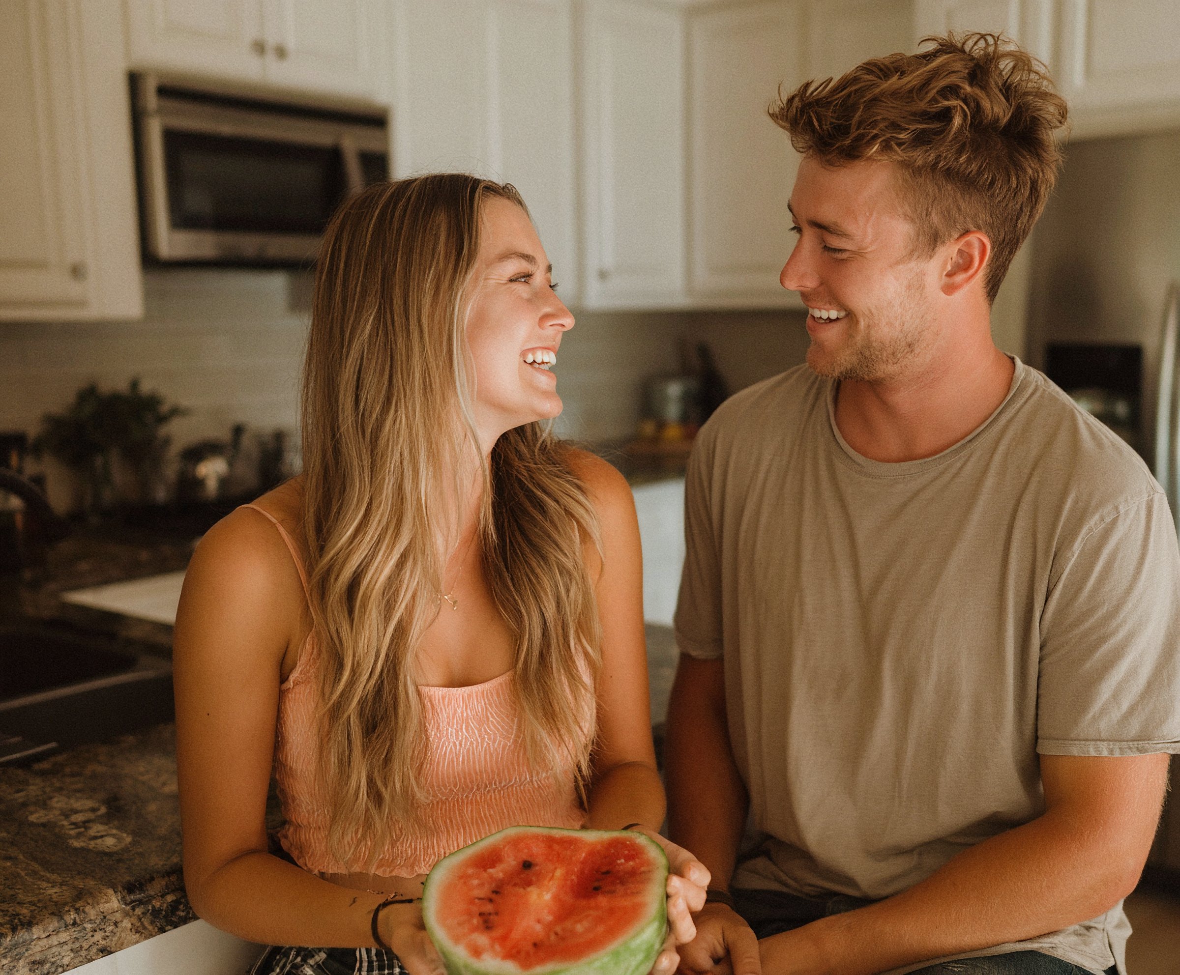 Couple laughing together in a kitchen, sharing watermelon